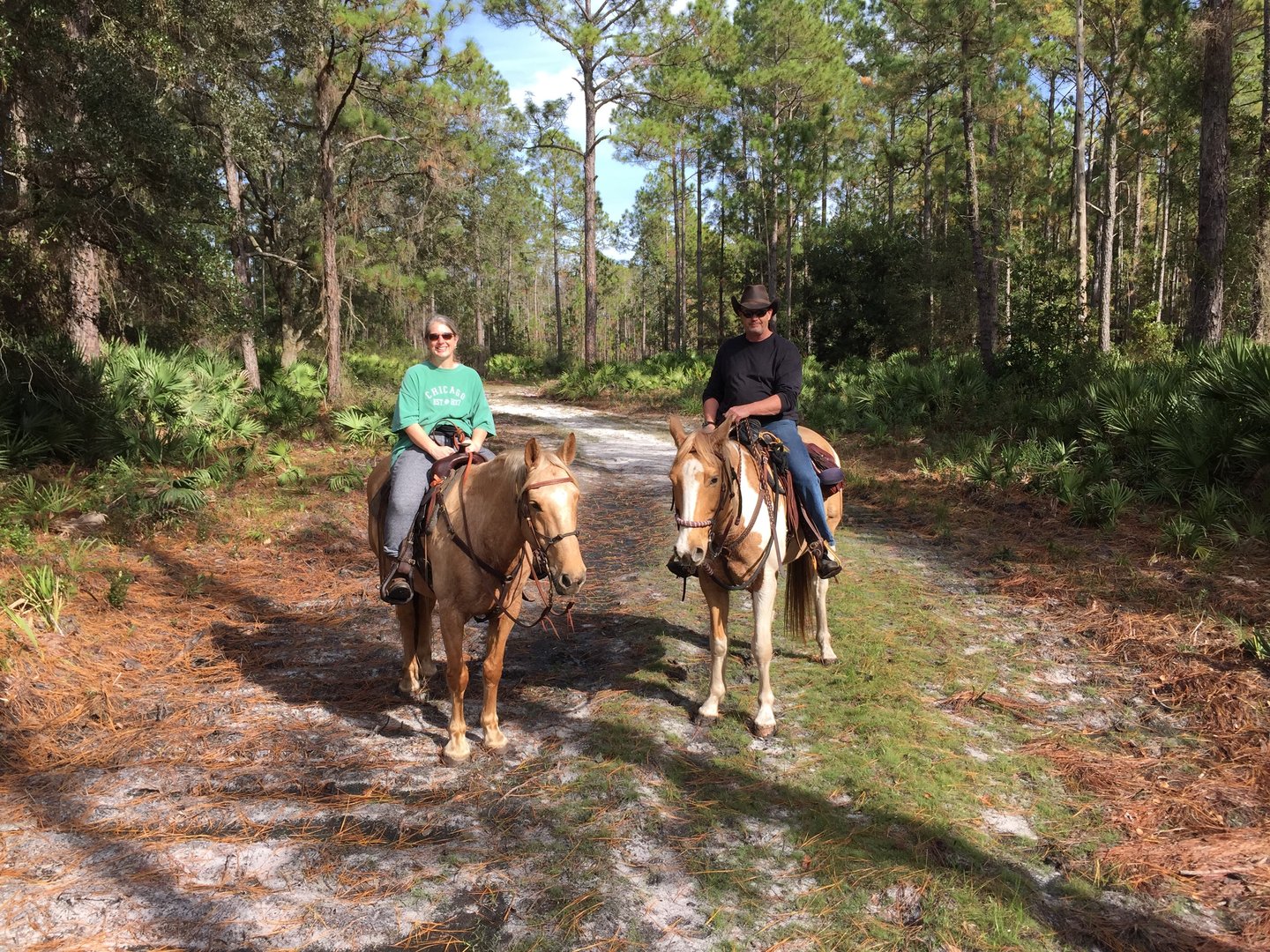 Two horseback riders on a wide park trail, the woman on the left and man on the right
