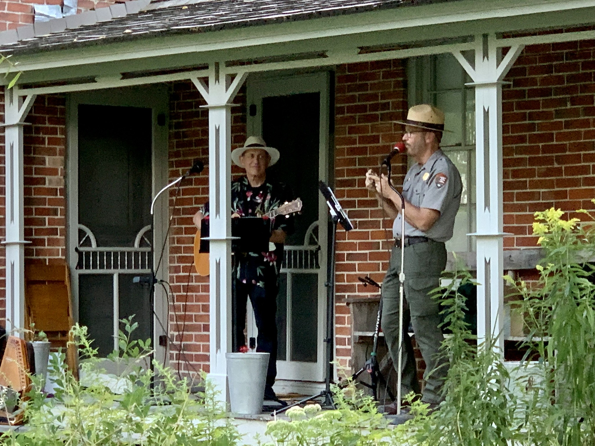 Two men on a porch playing guitar and storytelling